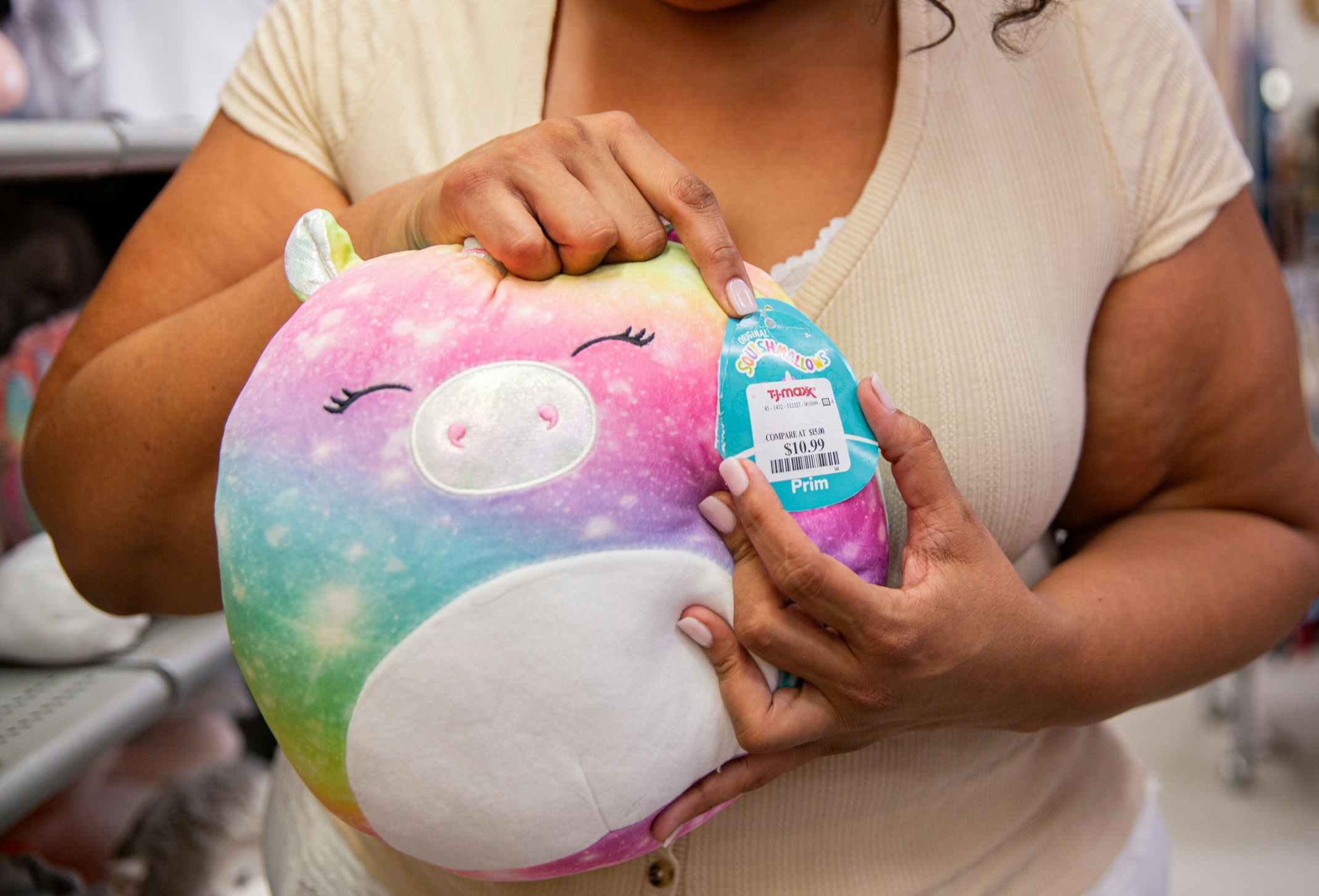 Person holding a rainbow squishmallow pointing to the brand tag with a tjmaxx sticker price on it 