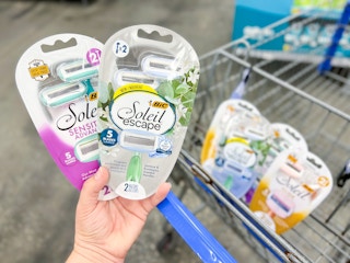 Hand holding razors with product in cart in background