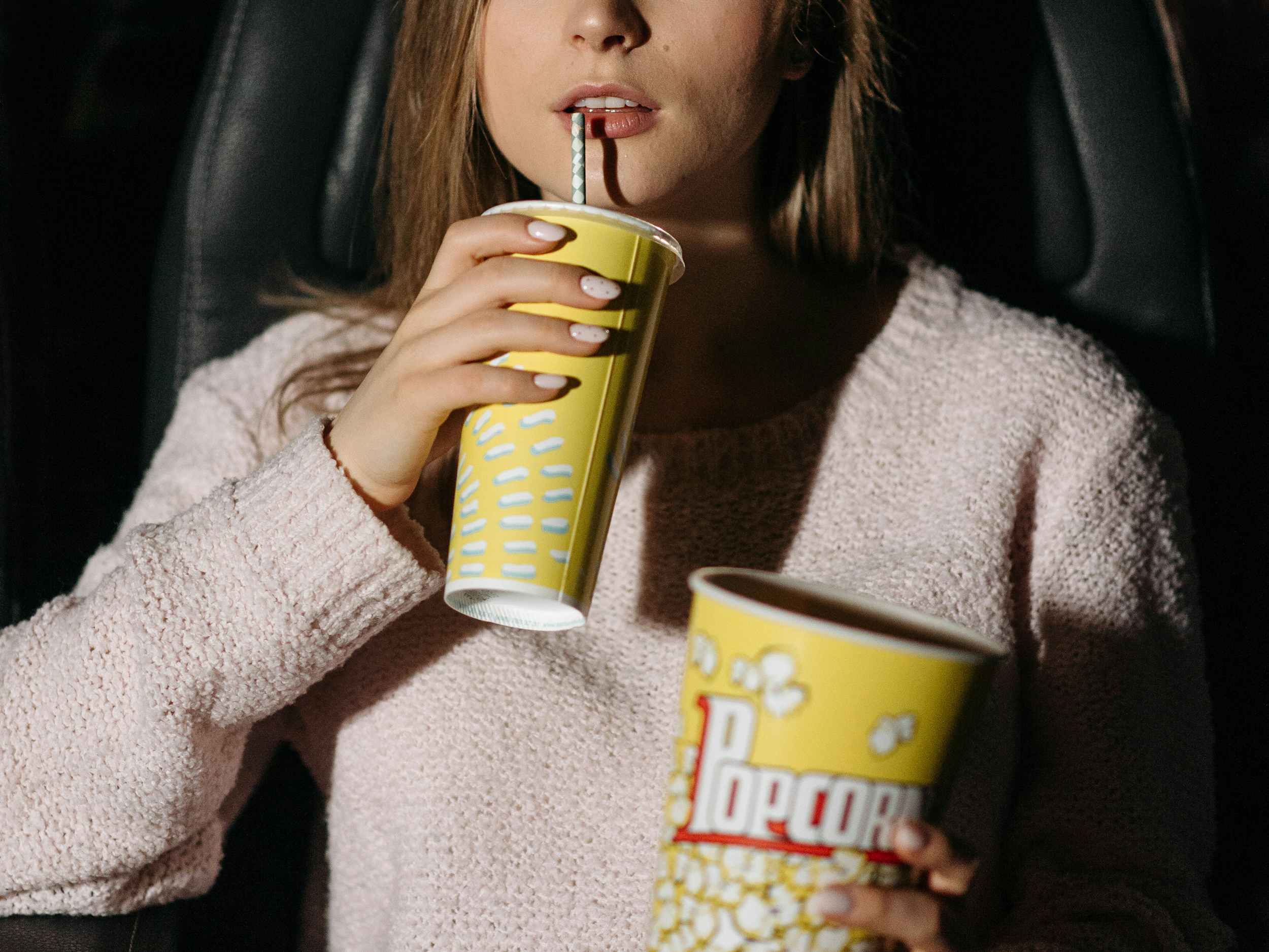 person in a movie theater drinking a soda and holding popcorn