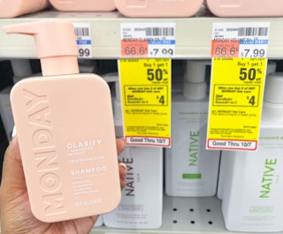 person holding a bottle of Monday shampoo next to sales tag