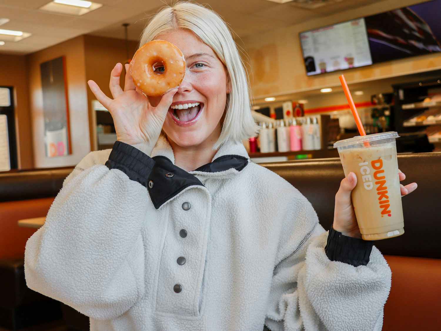 a person holding a donut and iced coffee at dunkin donuts