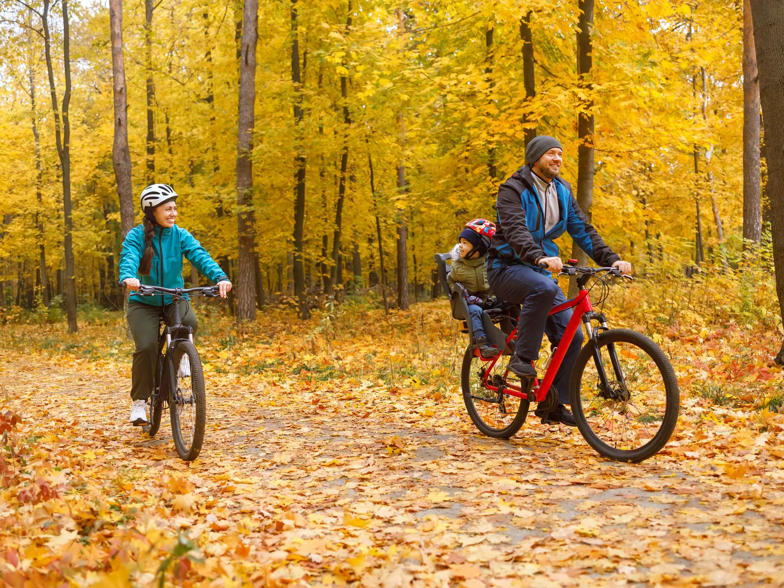 family of three taking a bike ride through the woods in the fall