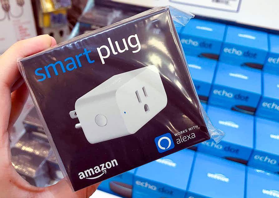 a person holding an amazon smart plug compatible with Alexa in front of a bunch of amazon echo dots on the shelf at Lowe's