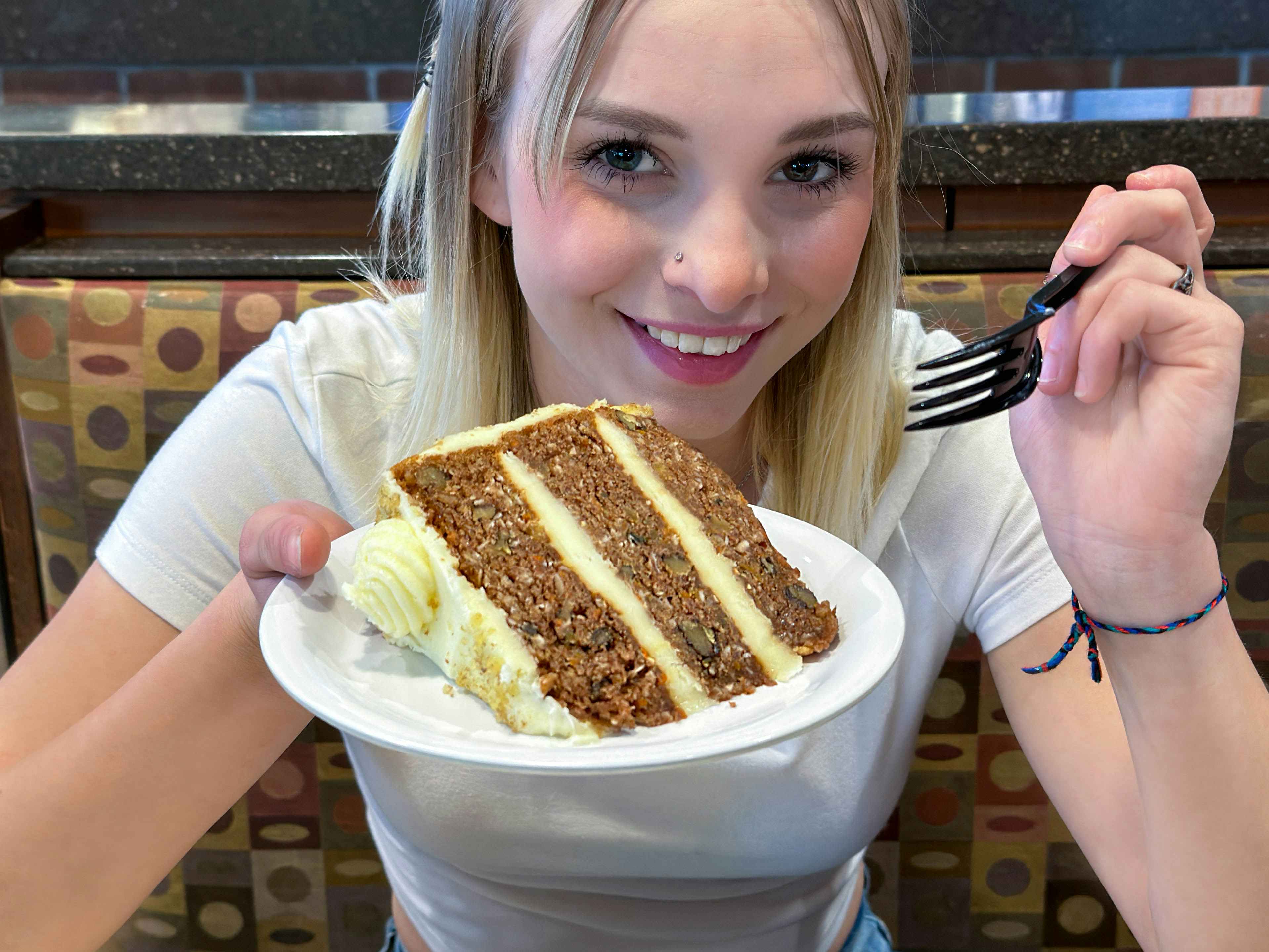  a woman holding up a piece of carrot cake and holding a fork 