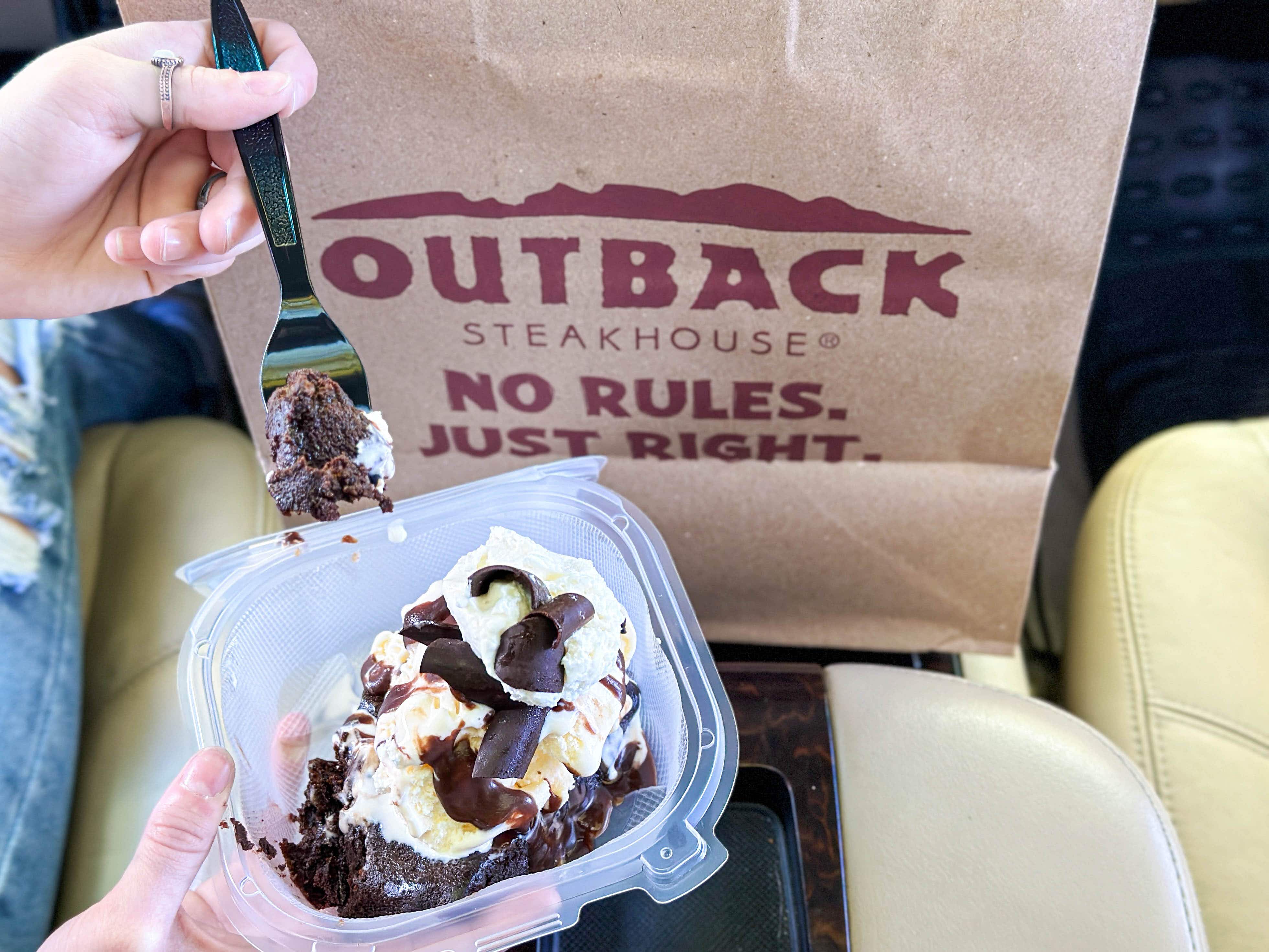a person sitting in a car eating ice cream and chocolate cake with a outback steakhouse take out bag 