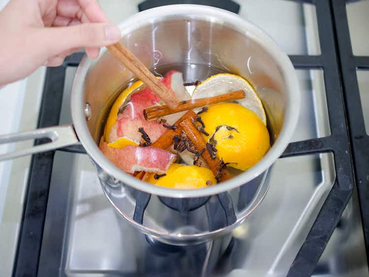 person brewing a diy potpourri on the stove with apple, lemon peels, and cinnamon