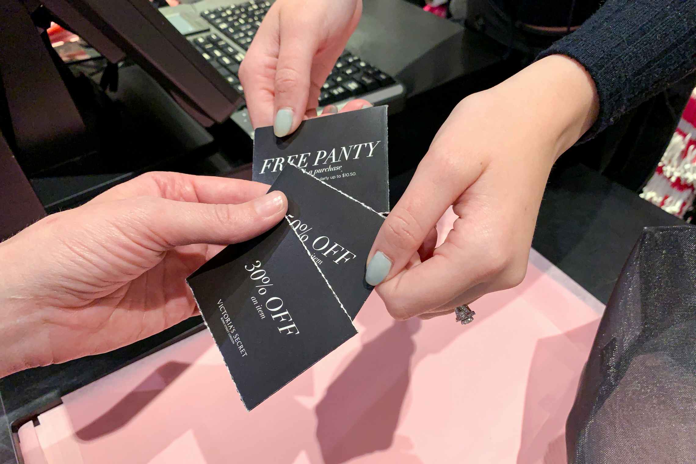 a Victoria's Secret employee handing some coupons to a customer at checkout