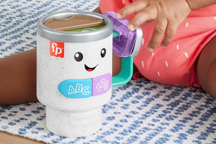 a child holding onto a fisher price coffee mug